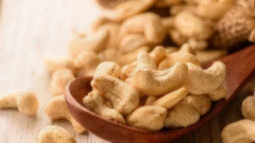 close up of cashew nuts in wood spoon on wood table