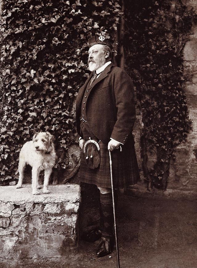 black and white photo of man in kilt with a dog