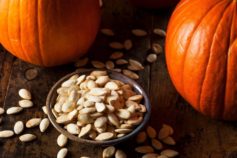 pile of pumpkin seeds next to pumpkins