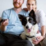 couple watching TV with their dog.